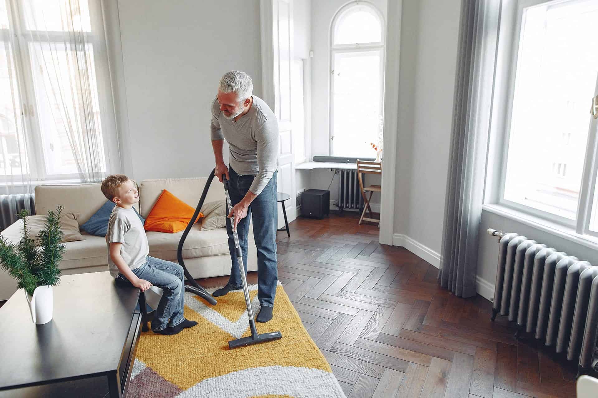 Grand-père nettoie le sol avec un aspirateur pendant que son petit-fils regarde.