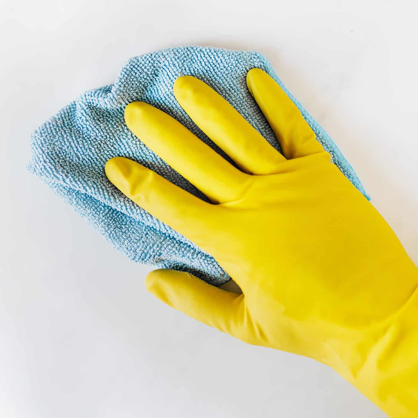 Femme nettoyant un mur avec un chiffon bleu et portant des gants jaunes.