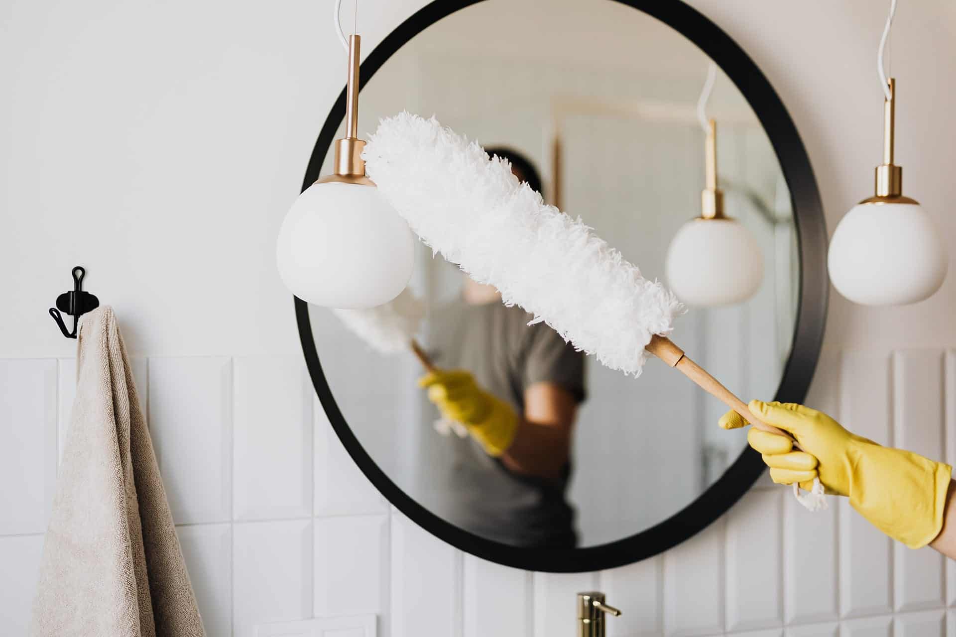 Femme nettoyant un mur et un miroir avec un plumeau en bois.