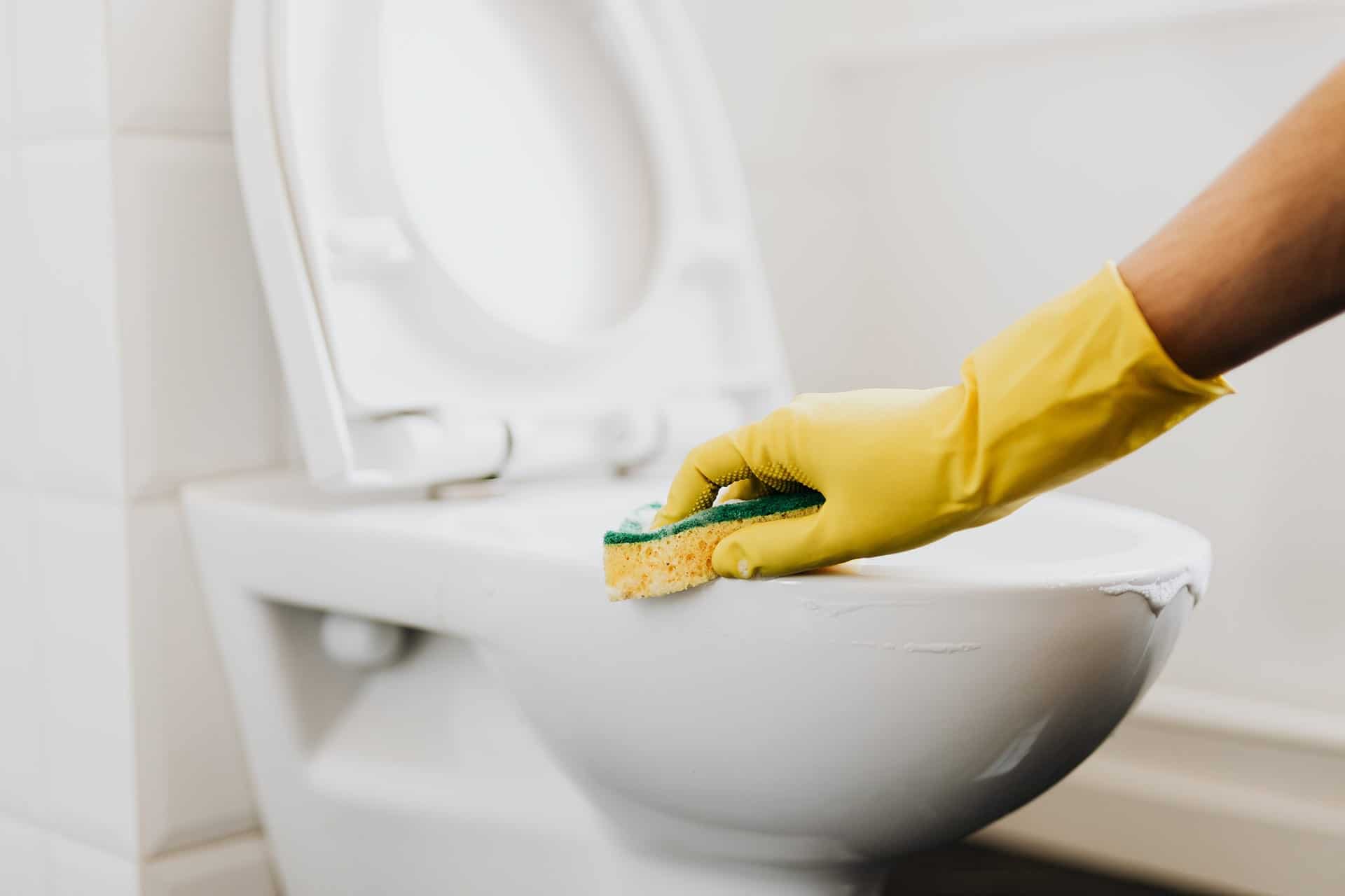 Femme portant des gants jaunes nettoyant un siège de toilette avec une brosse.