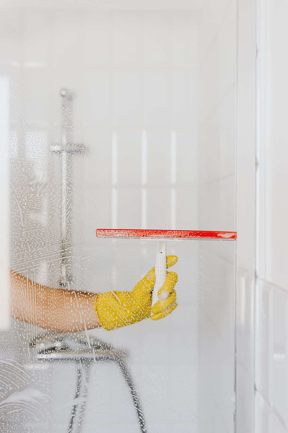 Femme portant des gants jaunes nettoie le miroir de la salle de bain avec un lave-vitre.