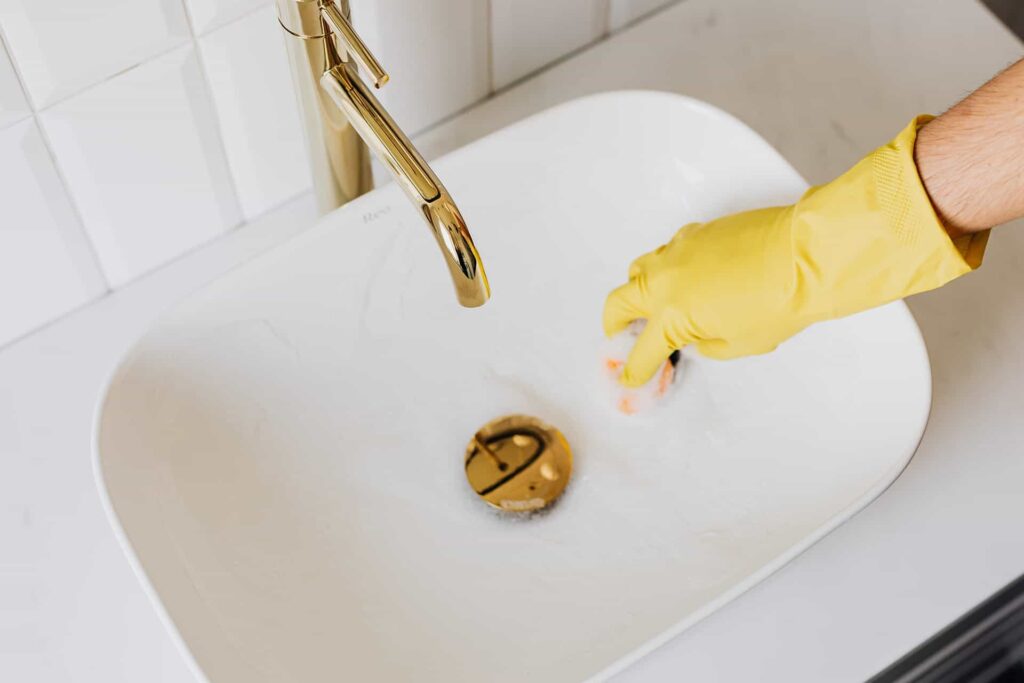 Femme portant des gants jaunes nettoie le lavabo.