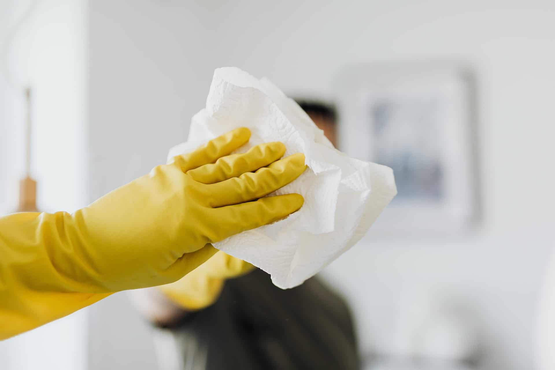 Femme portant des gants jaunes et nettoyant un miroir avec du papier.