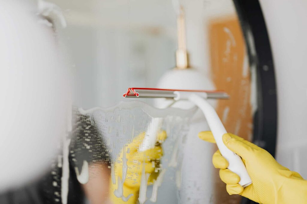 Femme nettoyant soigneusement un miroir avec un lave-vitre.