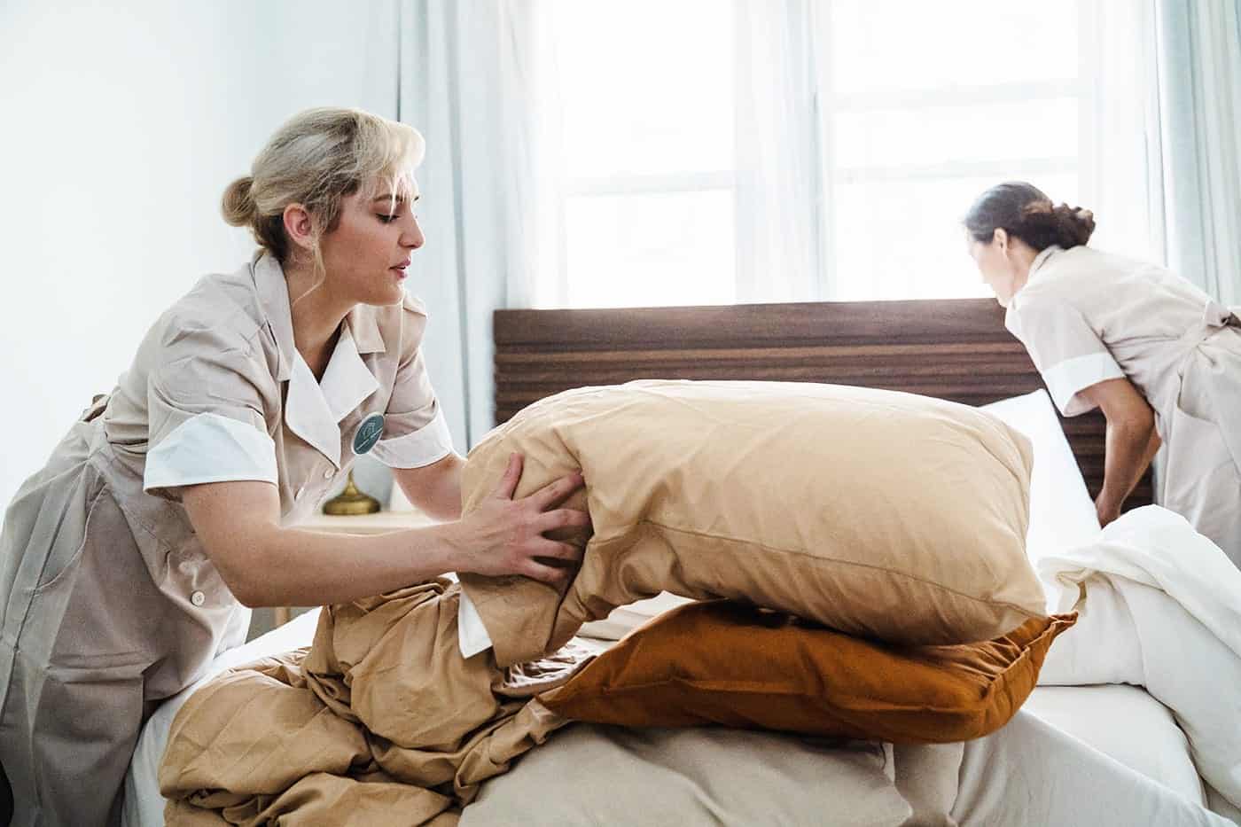 Deux femmes nettoyant une chambre, en train de faire le lit et organiser l'espace dans une pièce lumineuse et propre.